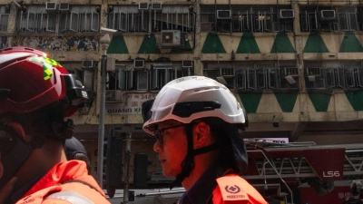 Im Hintergrund ist das ausgebrannte Hochhaus in Hongkong zu sehen - bei der Feuerwehr waren zahlreiche Hilferufe eingegangen. (Foto: Louise Delmotte/AP)