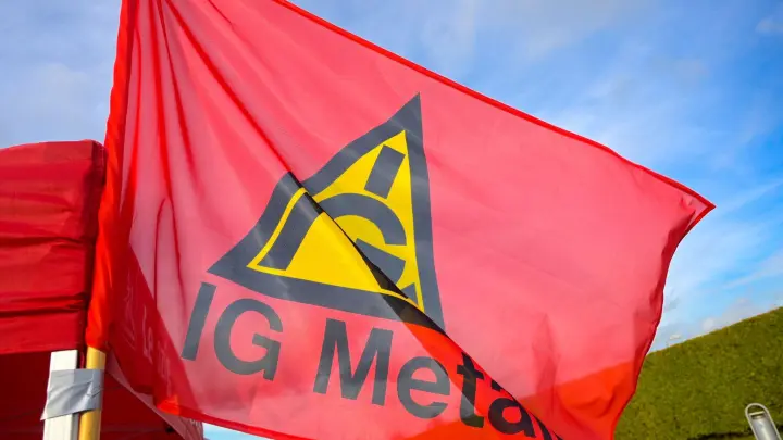 Eine Fahne mit dem Logo der IG Metall weht an einem Stand. (Foto: Heiko Rebsch/dpa/Symbolbild)