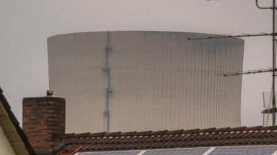 Wasserdampf steigt aus dem Kühlturm des Kernkraftwerks Isar 2, der hinter einem Wohnhaus mit Solarpanelen auf dem Dach zu sehen ist. (Foto: Peter Kneffel/dpa)