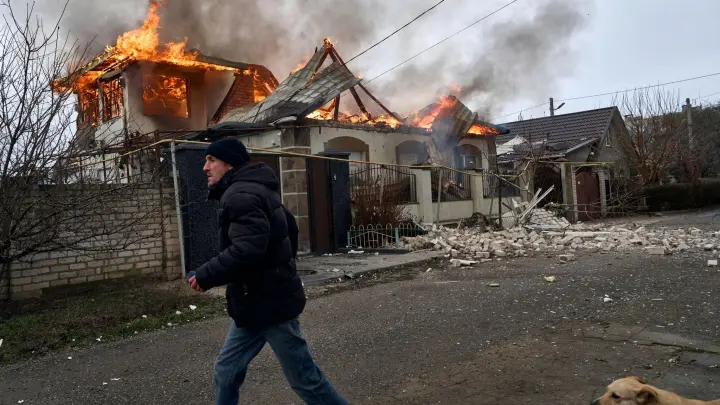 Ein Anwohner läuft an einem brennenden Haus in Cherson vorbei, das nach ukrainischen Angaben bei russischem Beschuss am orthodoxen Weihnachtsabend getroffen wurde. (Foto: Libkos/AP/dpa)