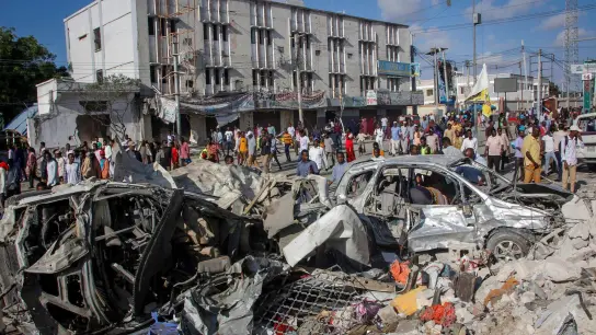 Menschen gehen an zerstörten Autos und Häusern vorbei. Mindestens 100 Menschen sind bei einem Anschlag getötet und 300 verletzt worden. (Foto: Farah Abdi Warsameh/AP/dpa)