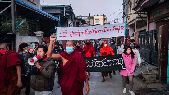 Junge Aktivisten und buddhistische Mönche nehmen an einer Protestkundgebung gegen die Militärregierung teil, während sie ein Transparent halten, auf dem in burmesischer Sprache steht: „Wer wagt es, auf der anderen Seite des Volkswillens zu stehen.“ (Foto: Uncredited/AP Photo/dpa)