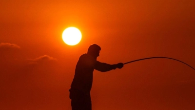 Alltag im Libanon: Ein Fischer wirft seine Angel von einem felsigen Gebiet entlang der Küste von Beirut aus, während die Sonne über dem Mittelmeer untergeht. (Foto: Hassan Ammar/AP/dpa)