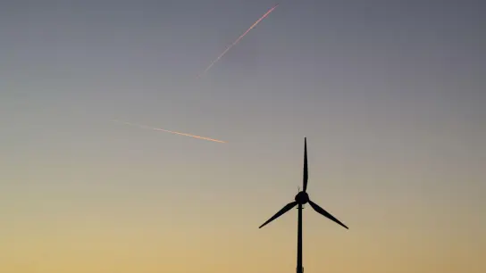 Zwei Flugzeuge ziehen Kondensstreifen am Himmel über einer Windkraftanlage. (Foto: Julian Stratenschulte/dpa/Archivbild)