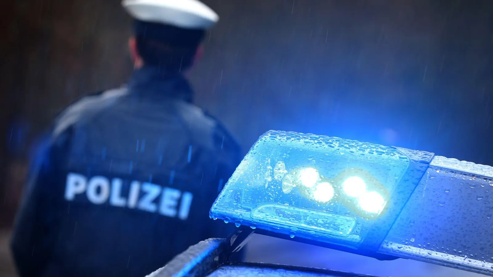 Ein Polizist steht im Regen vor einem Streifenwagen. (Foto: Karl-Josef Hildenbrand/dpa/Symbolbild)