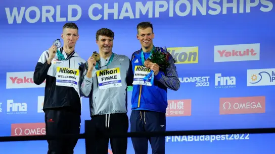 Der Zweitplatzierte Florian Wellbrock (l-r), Sieger Bobby Finke aus den USA, und der Ukrainer Michailo Romantschuk auf dem Podium. (Foto: Petr David Josek/AP/dpa)