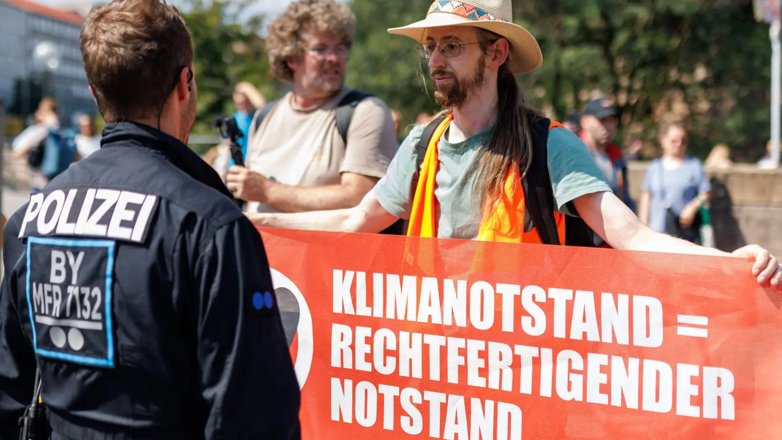 Ein Aktivist (r.) der Klimaschutzorganisation „Letzte Generation“ protestiert vor dem Nürnberger Hauptbahnhof. (Foto: Daniel Karmann/dpa)