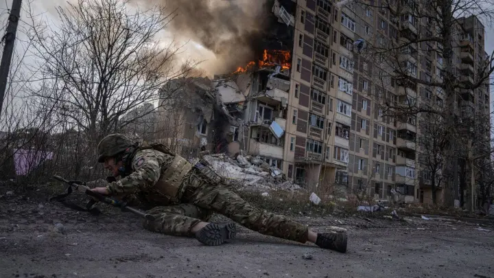 Ein ukrainischer Polizist geht in Awdijiwka vor einem brennenden Gebäude in Deckung. (Foto: Evgeniy Maloletka/AP)