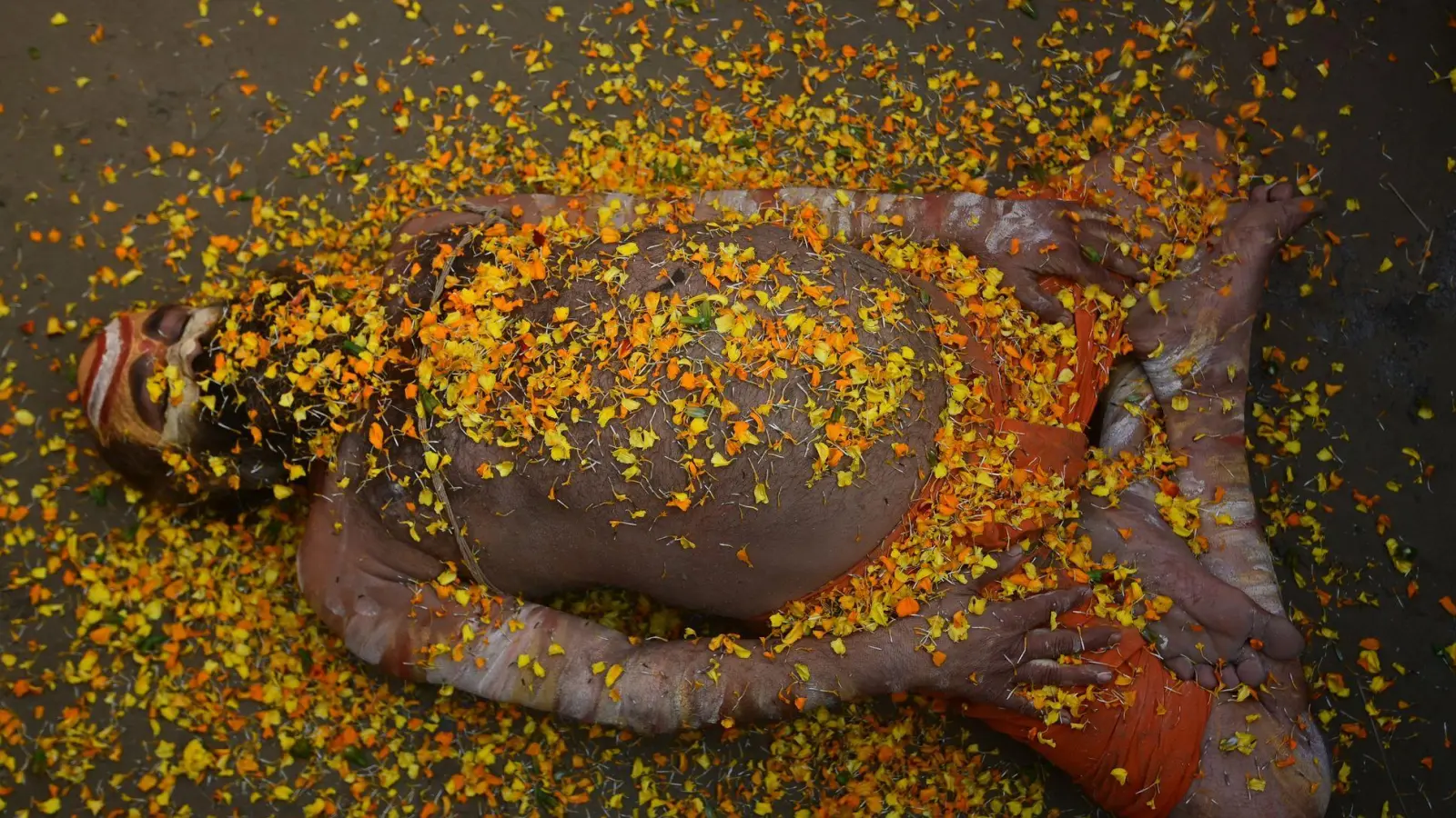 Bei einem hinduistischen Frühlingsfest in Indien liegt ein Sadhu mit Blütenblättern bedeckt auf der Straße.  (Foto: Prabhat Kumar Verma/ZUMA Press Wire/dpa)