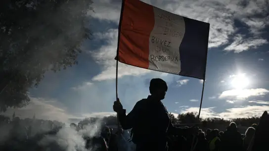 Ein Mann hält eine französische Nationalflagge mit der Aufschrift „Winzer in Gefahr - trinkt Bordeaux-Wein“ hoch. (Foto: Philippe Lopez/AFP/dpa)
