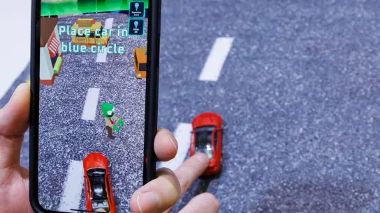 Mittels Smartphone, welches ein reales Spielzeugauto mit der Kamera erfasst, wird beim Spiel „Zombie Crasher AR“ von Augmented Robotics eine virtuelle Straßenszene dargestellt. (Foto: Daniel Karmann/dpa)