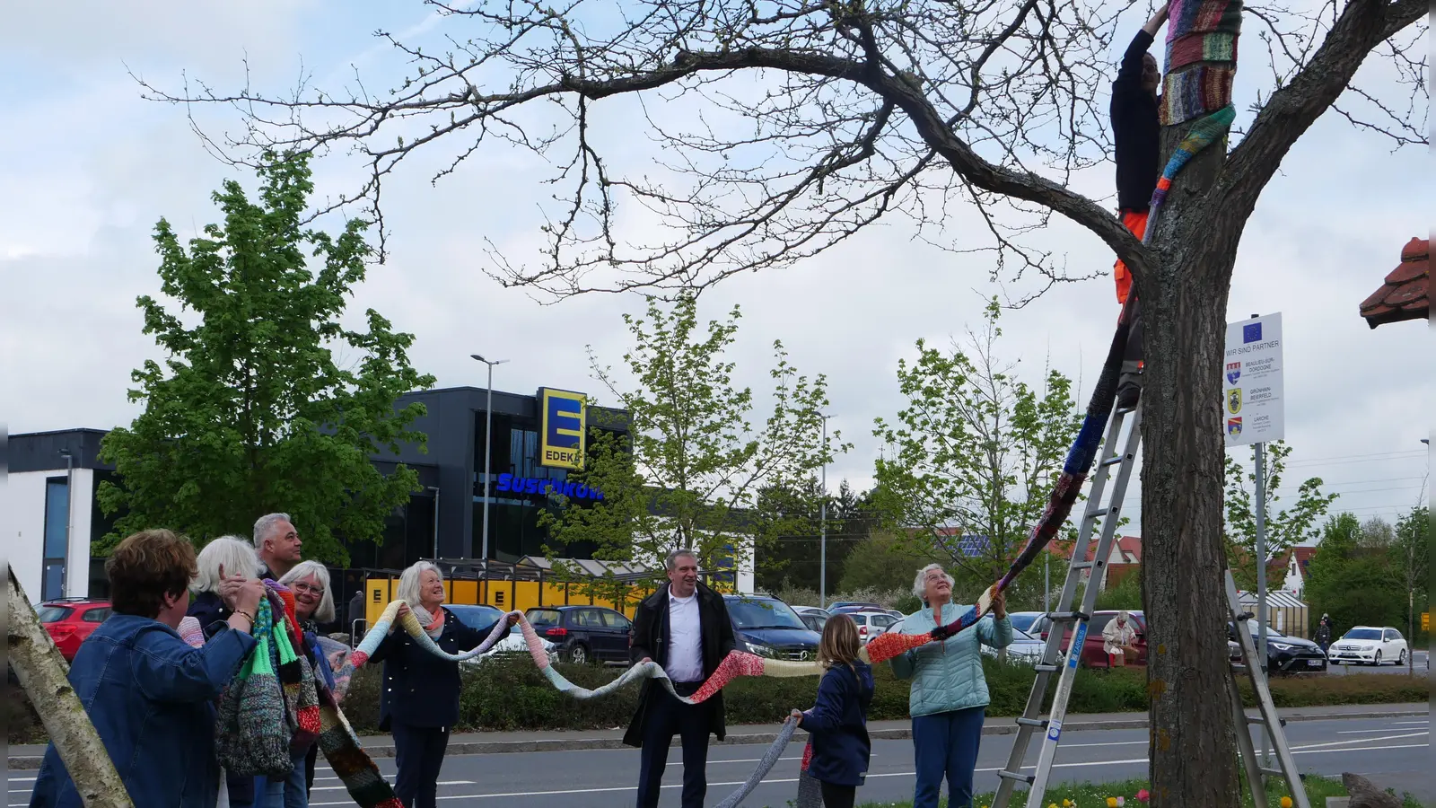 Gemeinsam wird der über 25 Meter lange Glücksschal am Baum am Ortseingang angebracht – mit tatkräftiger Unterstützung aus Nachbarschaftshilfe, Stadtverwaltung und Bauhof.<br><br>  (Foto: Martina Hinkelmann)