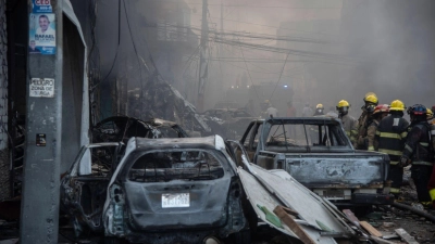 Feuerwehrleute arbeiten neben zerstörten Fahrzeugen nach einer starken Explosion, die ein Marktviertel mit vielen Geschäften erschüttert hat. (Foto: Jolivel Brito/AP/dpa)