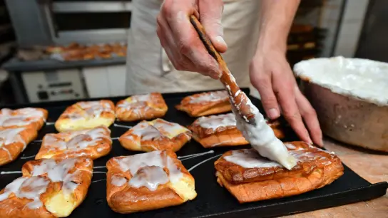 Ein Bäckermeister pinselt Zuckerguss auf süßes Gebäck in seiner Backstube. (Foto: Martin Schutt/dpa-Zentralbild/dpa)