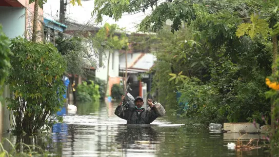 Ein Mann watet in der Provinz Ubon Ratchathani im Nordosten Thailands durch Wasserfluten. Heftige Regenfälle und starke Winde hatten in mehreren Gebieten Überschwemmungen ausgelöst. (Foto: Nava Sangthong/AP/dpa)