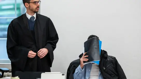 Der Mann, der wegen Vergewaltigung und Freiheitsberaubung an seiner Schwester angeklagt ist, verdeckt vor Beginn des Prozesses sein Gesicht, neben ihm sein Verteidiger Sandro Durante. (Foto: Silas Stein/dpa)