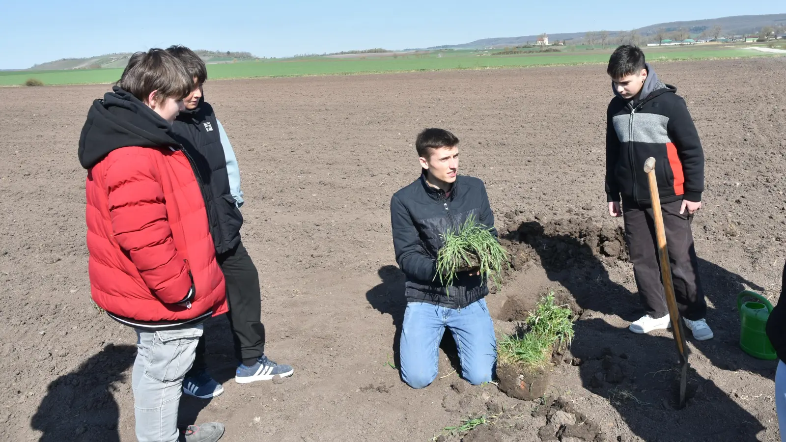 Jungbauer Markus Zeller erklärt drei Feldackerfrüchte. In der Hand hat er Weizen, am Boden sind Leguminosen und Gras. (Foto: Anita Dlugoß)