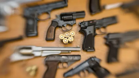 Pistolen und Revolver und Munition liegen auf einem Tisch in einer gesicherten Asservatenkammer. (Foto: Friso Gentsch/dpa/Symbolbild)