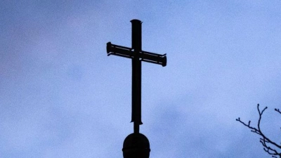 Dunkle Wolken über einem Kreuz einer Kirche: Einem der Missbrauchsopfer muss Schadenersatz gezahlt werden (Symbolbild). (Foto: Julian Stratenschulte/dpa)