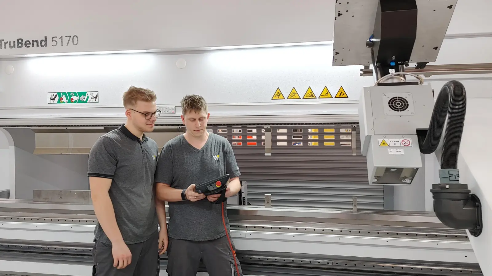 Oliver Schmidt (links) und Maxim Schlender geben die Befehle ein, im Hintergrund arbeitet fast mannlos eine neue, vollautomatische Blechbearbeitungsmaschine, die sich sogar ihr Material selbst holt. (Foto: Katrin Merklein)