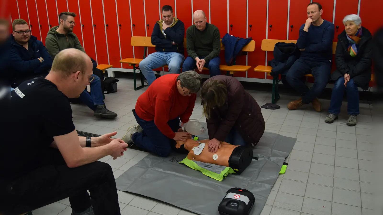 Teilnehmerinnen führen unter Anleitung von Daniel Strauß Beatmung und Herzdruckmassage bei einer Puppe durch und folgen den akustischen Anweisungen des Defibrillators. (Foto: Lucie Seidel)