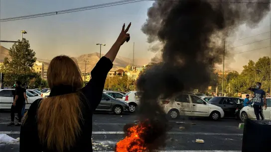 Nach dem Tod der 22-jährigen Mahsa Amini steht eine Frau während einer Demonstration in Teheran vor einem brennenden Autoreifen. (Foto: Uncredited/AP/dpa)