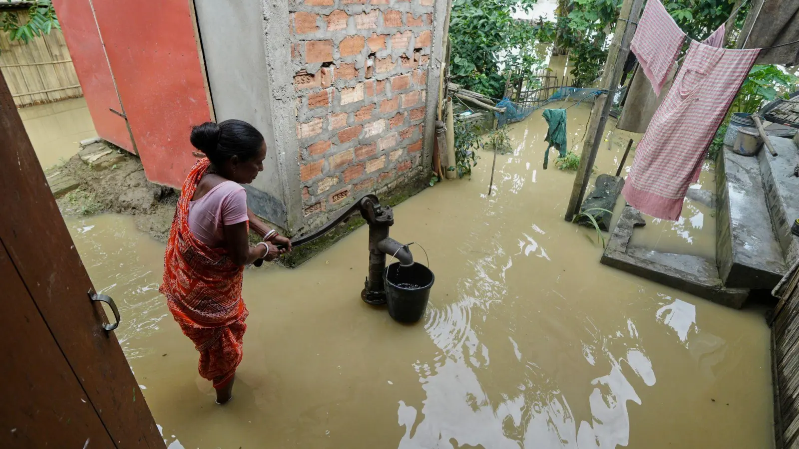 Eine Frau versucht in der überfluteten Umgebung ihres Hauses, Wasser zu sammeln.  (Foto: Uncredited/AP/dpa)