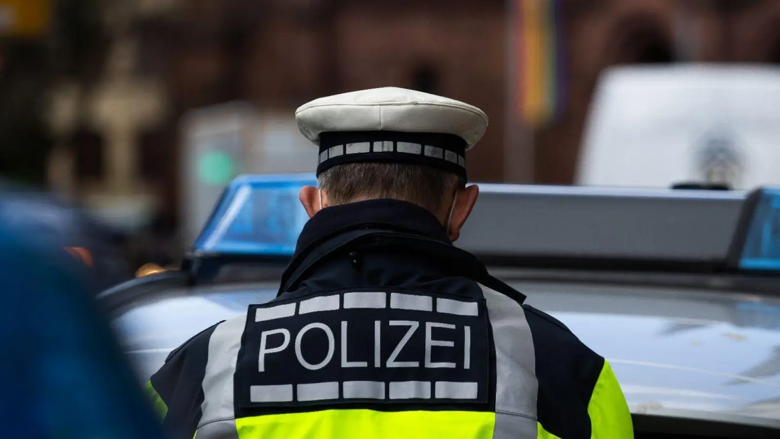 Ein Polizeibeamter steht zwischen zwei Einsatzfahrzeugen der Polizei. (Foto: Philipp von Ditfurth/dpa/Symbolbild)