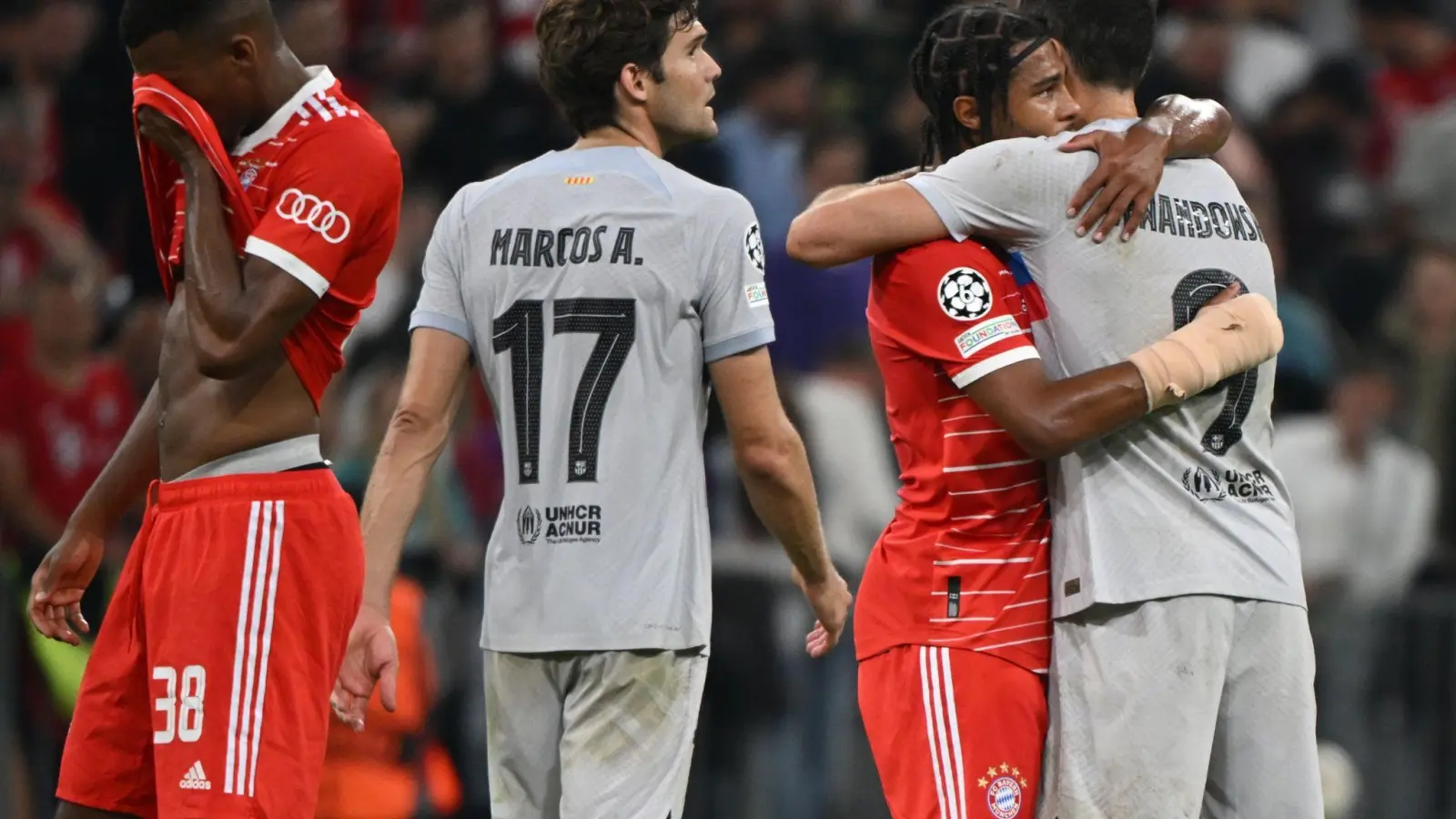 Barcelonas Robert Lewandowski (r)umarmt Münchens Serge Gnabry (2.v.r.) nach dem Spiel. Links steht Münchens Ryan Gravenberch, daneben Barcelonas Marcos Alonso. (Foto: Peter Kneffel/dpa)