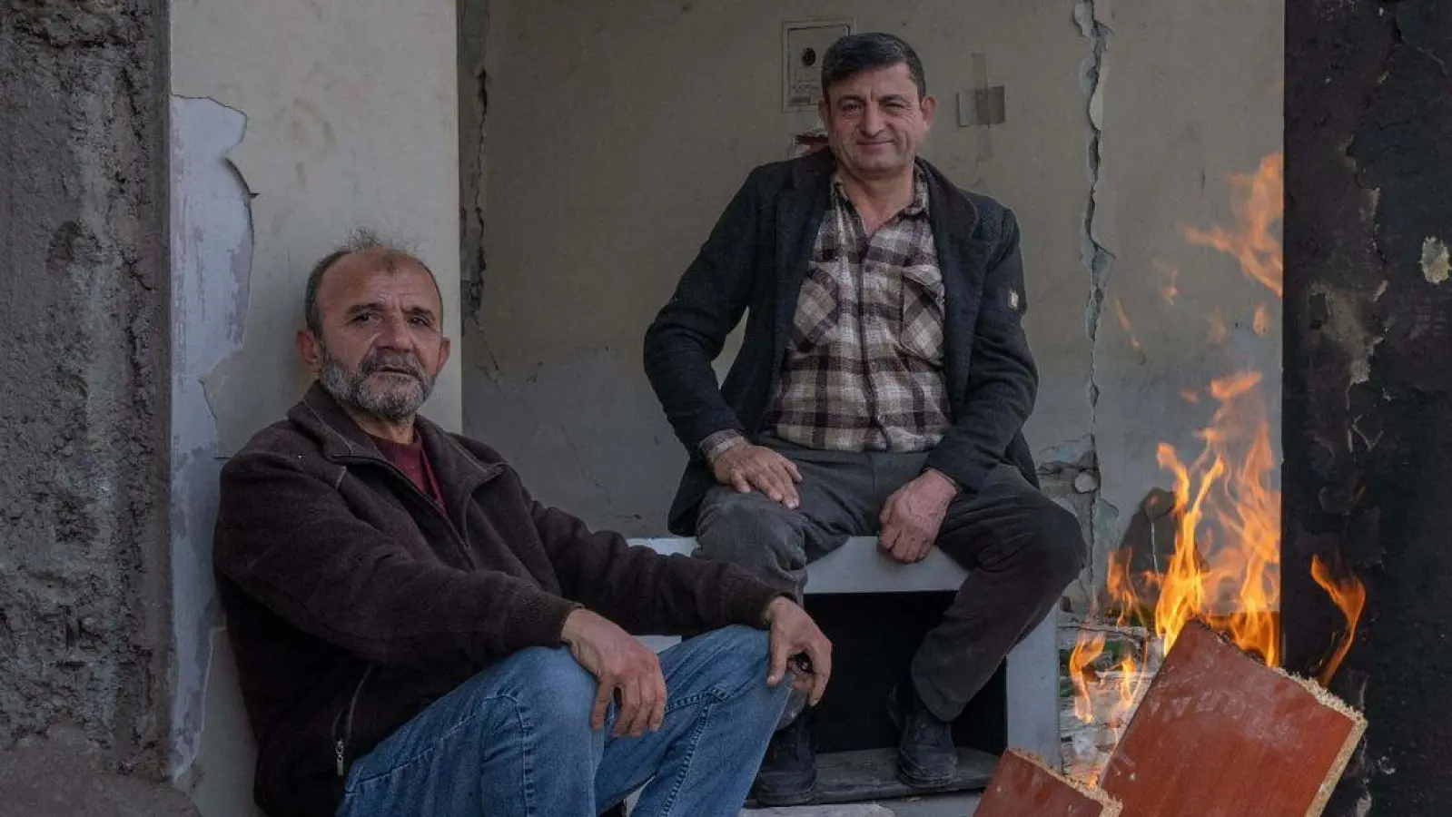 Zwei Männer wärmen sich in den Trümmern eines zerstörten Hauses in Kahramanmaras an einem Feuer. Im Zentrum der Stadt waren bei dem Beben vor einem Jahr unzählige Häuser zerstört oder beschädigt worden. (Foto: Boris Roessler/dpa)
