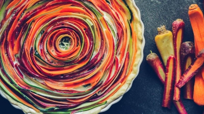 Ein echter Hingucker: Gehobelte Streifen von orangen, gelben und lila Möhren sowie einer Zucchini spiralförmig auf einem Mürbeteigboden mit Eier-Ziegenkäsegemisch legen und backen - fertig ist die Tarte. (Foto: Aileen Kapitza/minzgruen.com/dpa-tmn)
