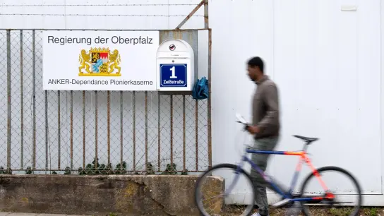 Ein Mann mit einem Fahrrad geht an einem Hinweisschild vom Ankerzentrum in der Zeißstraße vorbei. (Foto: Lino Mirgeler/dpa/Archivbild)
