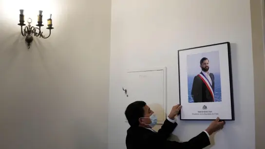 Ein Palastangestellter hängt das offizielle Porträt des neuen chilenischen Präsidenten Boric im Büro des Präsidentenpalastes La Moneda auf. (Foto: Matias Delacroix/AP/dpa)