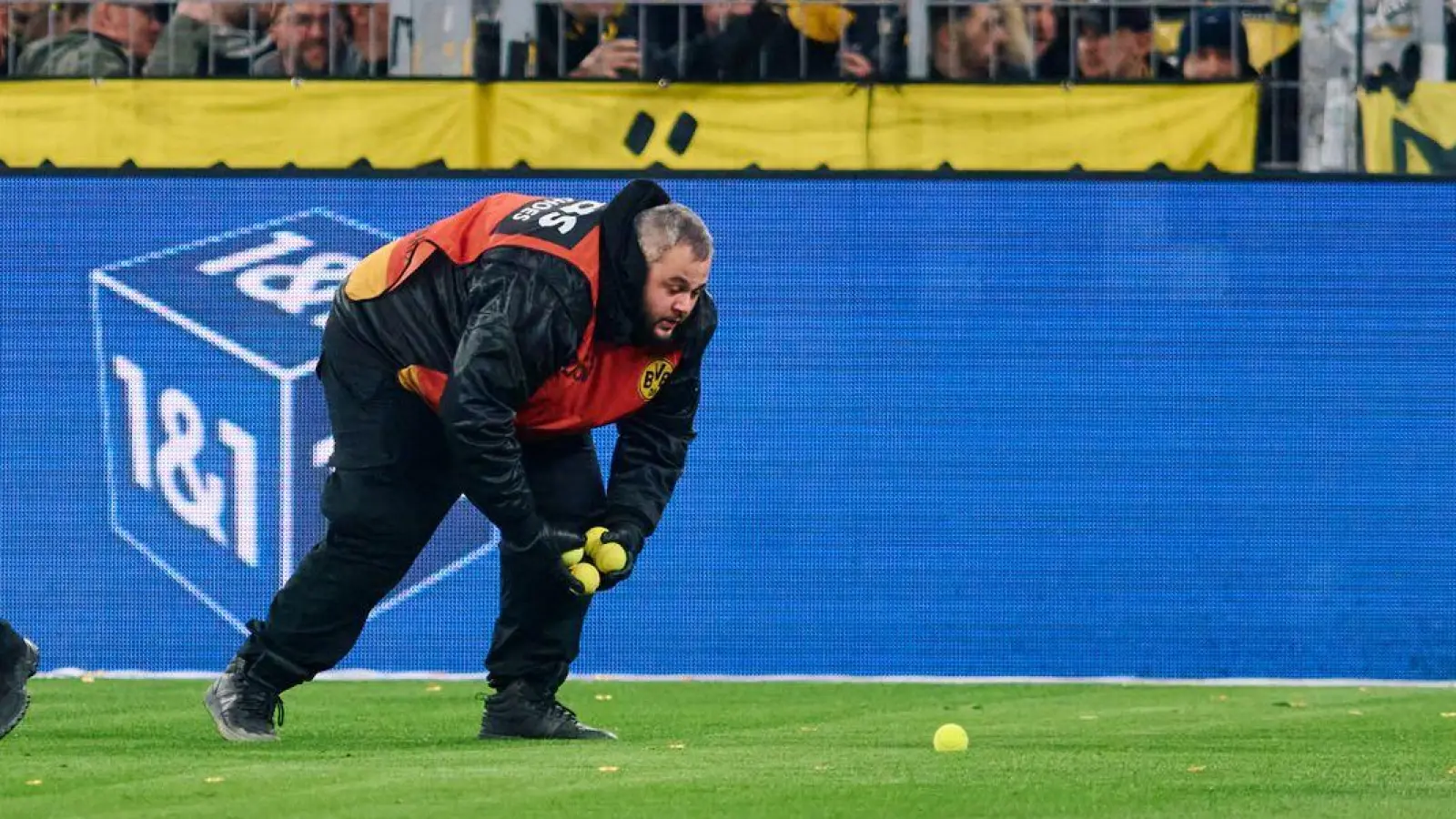 Stadionmitarbeiter sammeln Tennisbälle ein, die Fans auf das Spielfeld geworfen haben, um gegen Investoren in der DFL zu protestieren. (Foto: Bernd Thissen/dpa)