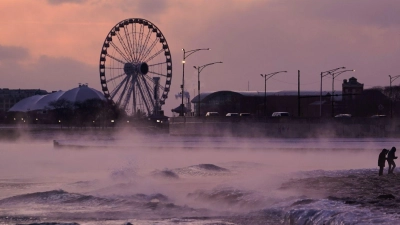 Menschen spazieren in Chicago über einen mit Eis bedeckten Strand am Ufer des Michigansees. (Foto: Kiichiro Sato/AP/dpa)