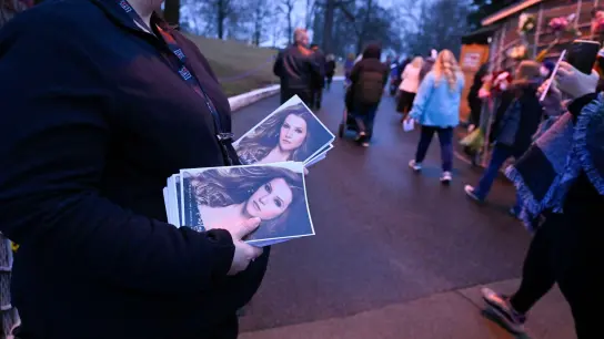 Eine Frau hält Flyer mit einem Bild von Lisa Marie Presley, während Menschen an ihr vorbeigehen, um in Graceland an einem Gedenkgottesdienst teilzunehmen. (Foto: John Amis/FR69715 AP/dpa)