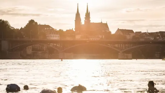 Panoramablick aufs Münster: Menschen treiben mit ihrem Wickelfisch in Basel den Rhein hinab. (Foto: Markus Buehler/Sitzerland Tourism/dpa-tmn)