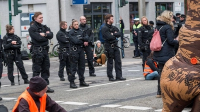 Demonstrantinnen und Demonstranten, die auf der Straße sitzen, blockieren die Kreuzung Kumpfmühler Str. und Fritz-Fend-Straße. (Foto: Daniel Vogl/dpa)