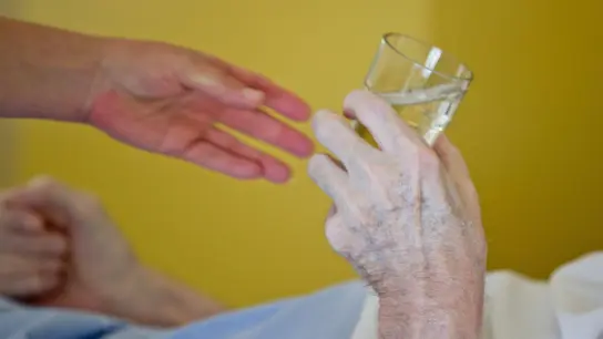 Eine Krankenpflegerin reicht einem Patienten ein Glas Wasser. (Foto: Daniel Karmann/dpa)