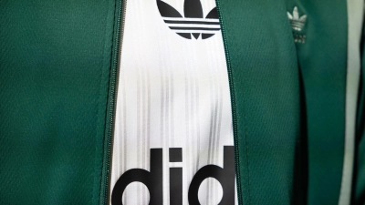 Das Logo und der Schriftzug von Adidas ist auf einem ausgestellten Kleidungsstück zu sehen. (Foto: Daniel Karmann/dpa/Symbolbild)