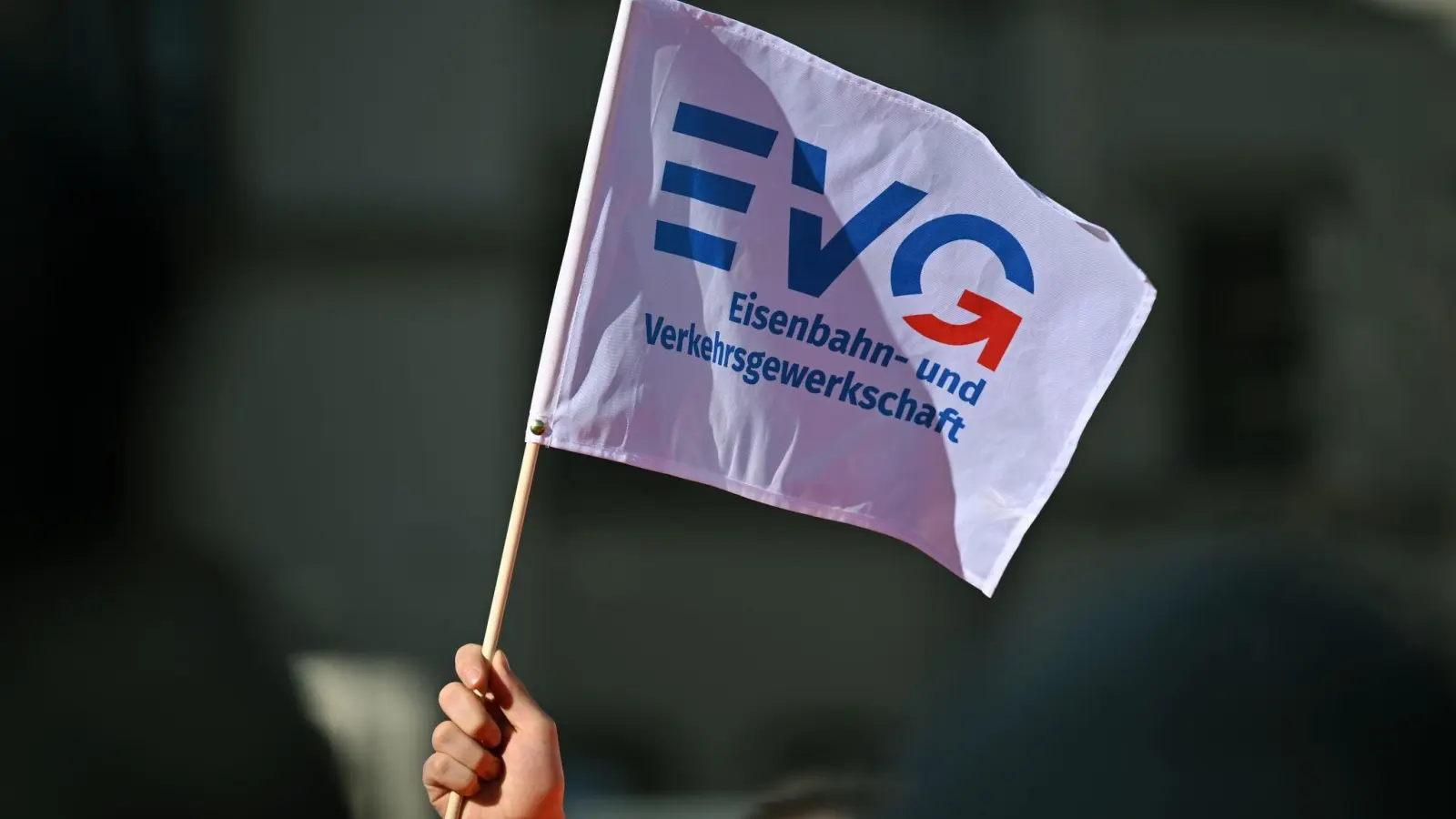Ein Teilnehmer am Warnstreik Ende März vor dem Erfurter Hauptbahnhof mit einem Fähnchen der Eisenbahn- und Verkehrsgewerkschaft (EVG). (Foto: Martin Schutt/dpa)