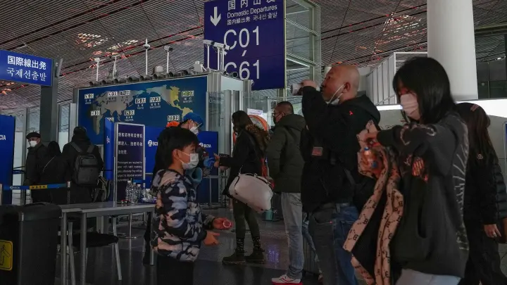 Passagiere mit Mund-Nasen-Schutz stehen am Flughafen Peking an der Sicherheitskontrolle vor einem internationalen Abfluggate an. (Foto: Andy Wong/AP/dpa)