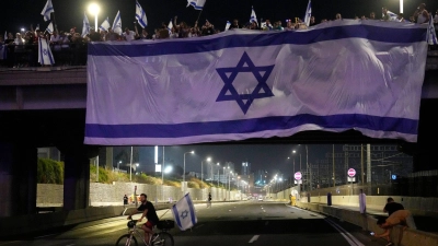 Demonstranten haben bei ihren Protesten eine riesige Nationalfahne an einer Autobahnüberführung in Tel Aviv aufgehängt. (Foto: Ariel Schalit/AP)