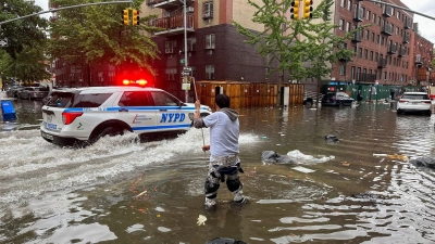 Hochwasser auf den Straßen von New York: Im Stadtteil Brooklyn versucht ein Mann, mit einem  Stock einen Abfluss zu reinigen, während ein Polizeiwagen vorbeifährt. (Foto: Jake Offenhartz/AP/dpa)