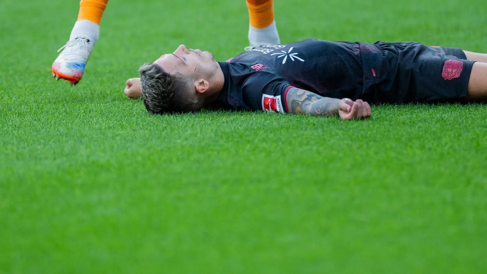 Bayer Leverkusens Kapitän Alejandro Grimaldo liegt nach einem Zusammenprall mit dem eigenen Mann benommen auf dem Boden.  (Foto: Rolf Vennenbernd/dpa)