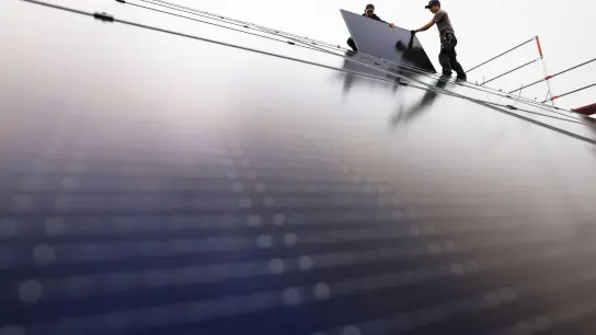 Handwerker montieren auf dem Dach eines Wohnhauses Solarmodule. (Foto: Oliver Berg/dpa)