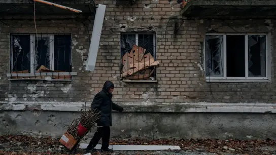Ein Mann trägt Reisig für einen Holzofen zum Keller eines Wohnhauses, der als Bunker genutzt wird. (Foto: Libkos/AP/dpa)