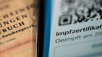 Ein Smartphone, auf dem ein Impfzertifikat angezeigt wird, liegt auf einem Impfbuch. (Foto: Marijan Murat/dpa/Symbolbild)
