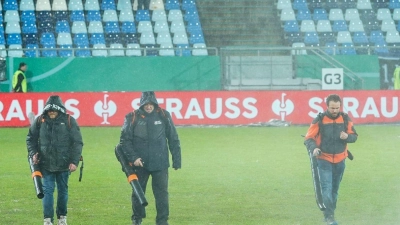 Helfer versuchen, Wasserlachen vom Spielfeld zu entfernen. (Foto: Uwe Anspach/dpa)