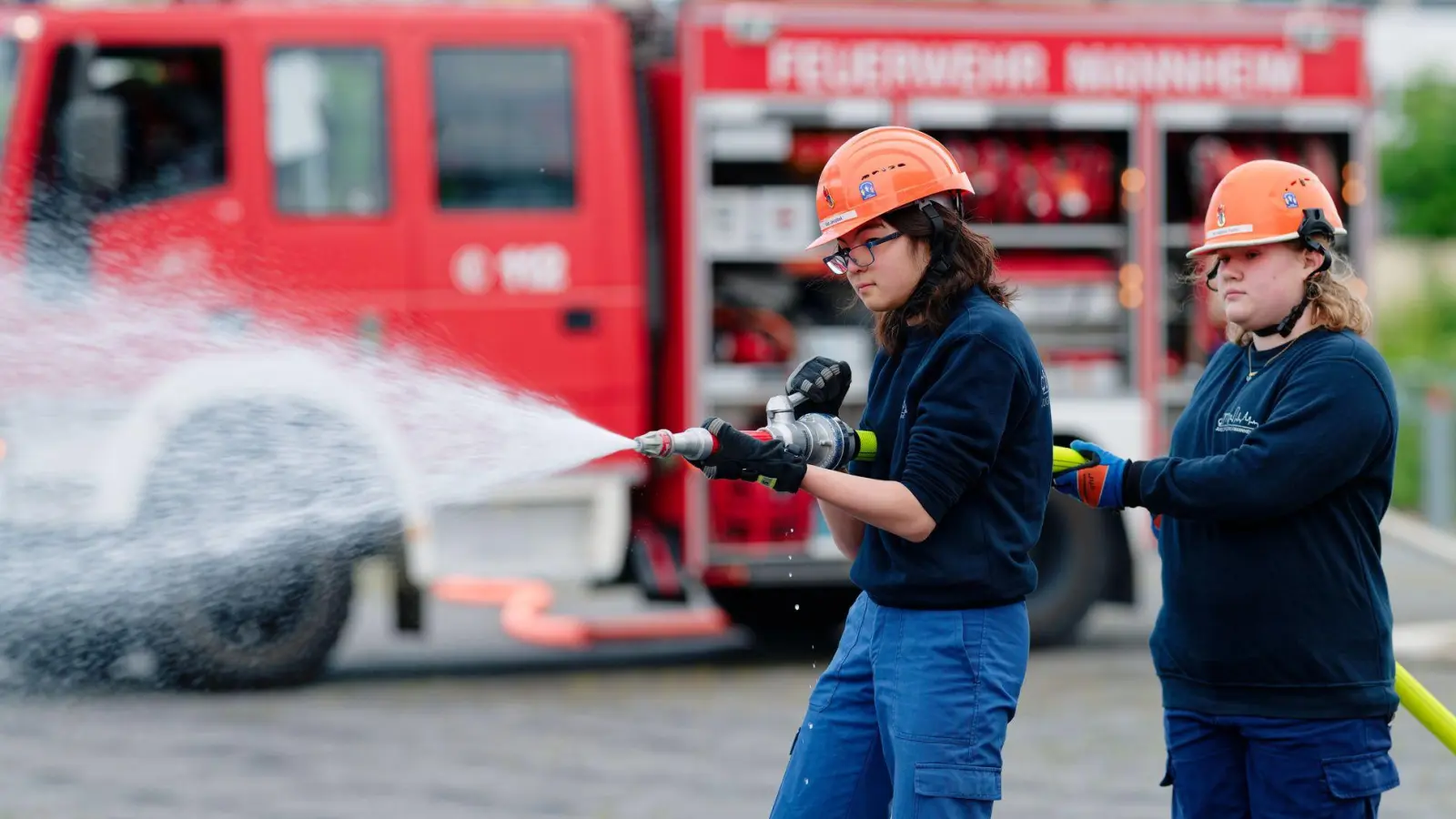 Ilias (links) und Annabella, Mitglieder der Jugendfeuerwehr in Mannheim, halten bei einer Übung einen Feuerwehrschlauch in den Händen. (Foto: Uwe Anspach/dpa)